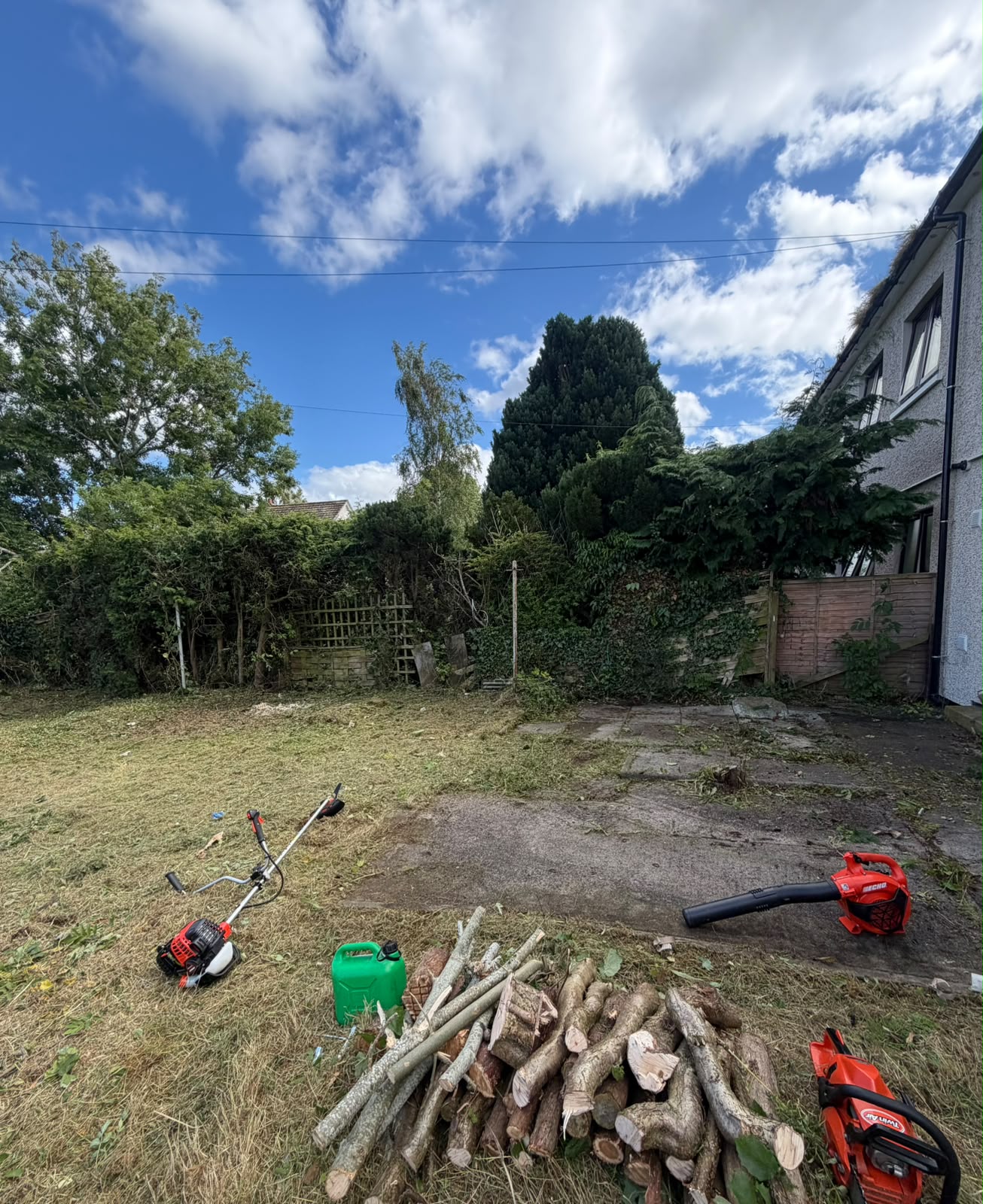 Garden clearance in progress in the Highlands, strimmed grass, cut logs stacked and waste ready for removal